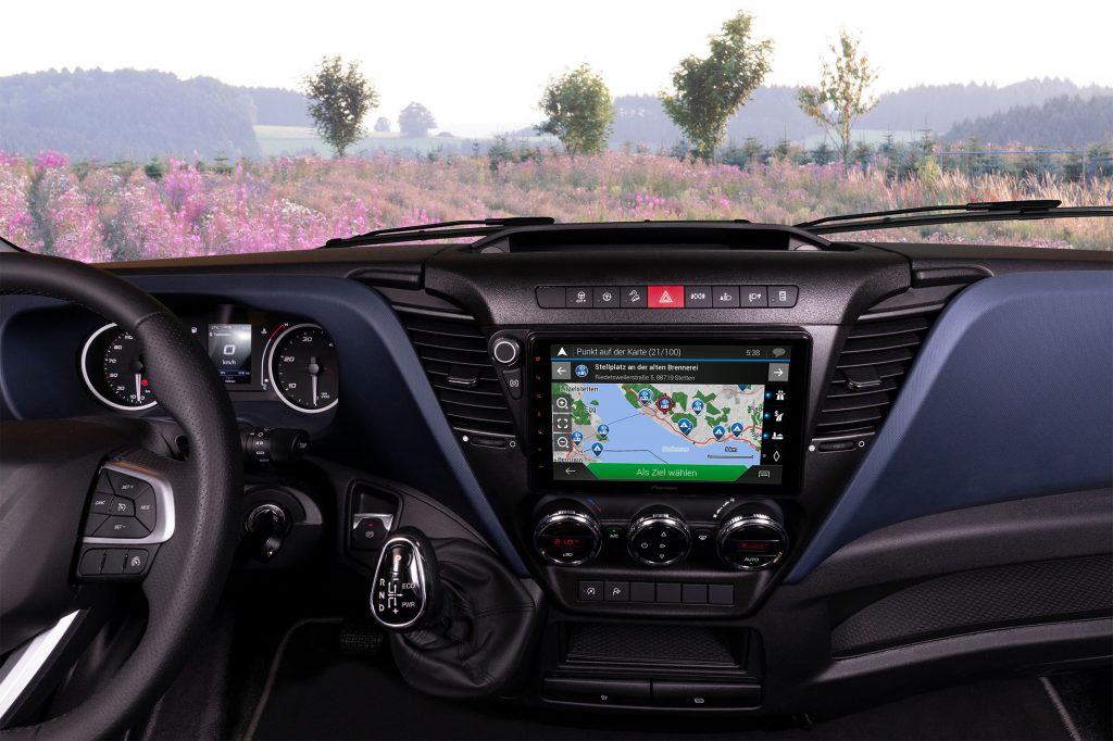 Armaturenbrett eines Iveco Daily mit eingebautem Pioneer Mediacenter AVIC-Z1000DAB. Durch die Windschutzsscheibe ist eine im Nebel liegende Landschaft zu sehen, im Vordergrund ein lilafarbenes Lavendelfeld und vier einzelne kleine Bäume. Der Bildschirm des AVIV-Z1000DAB zeigt eine Navigationsansicht.